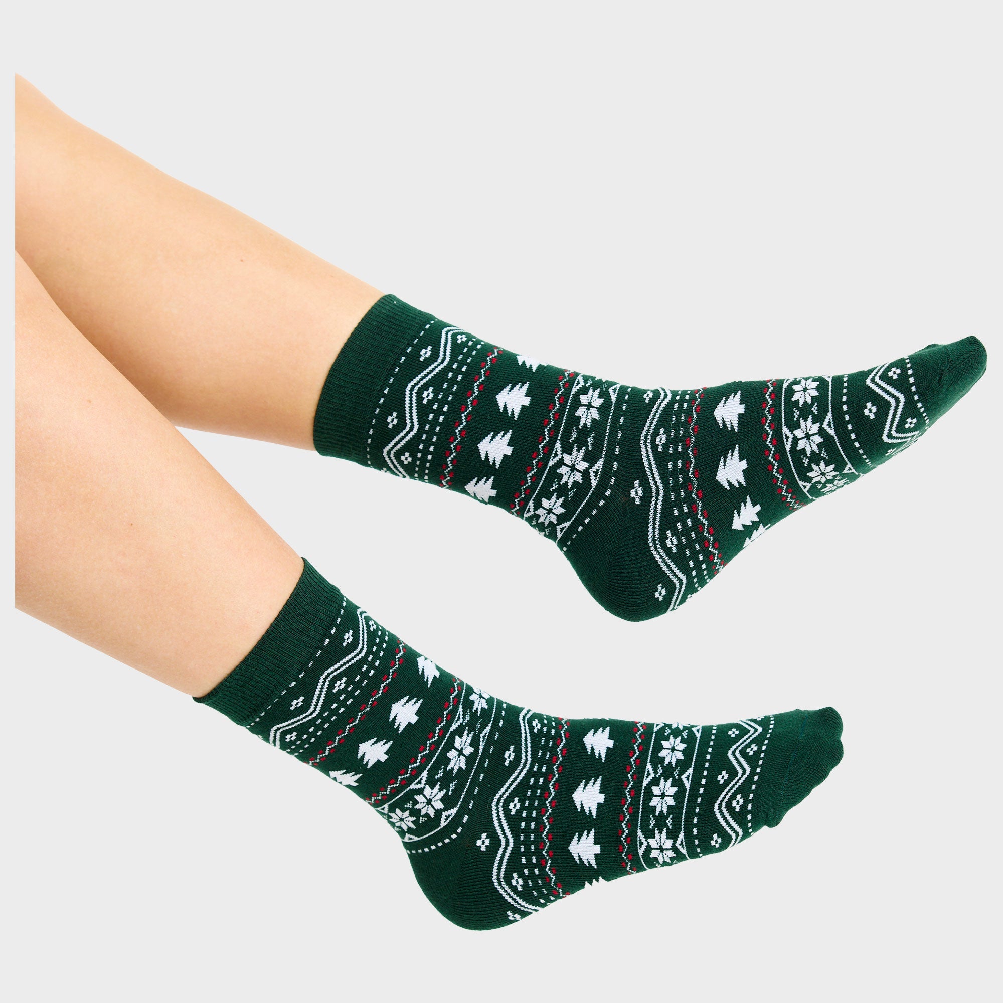 Een paar benen met een paar groene kerstsokken met kerstbomen erop.