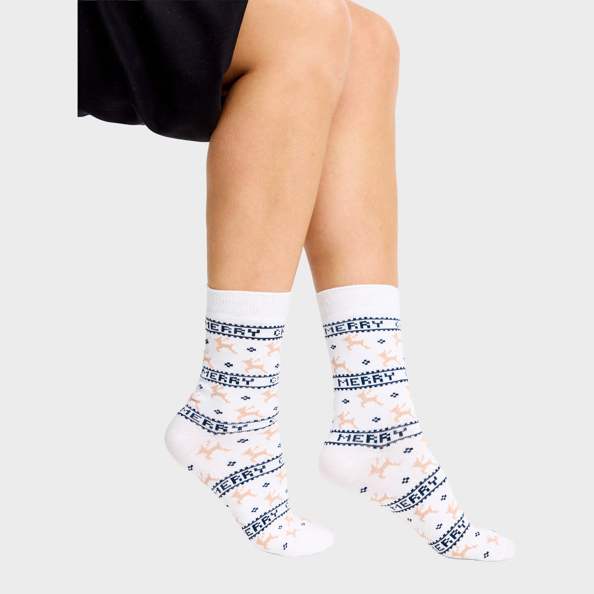 Een paar voeten met witte kerstsokken met rendieren erop.