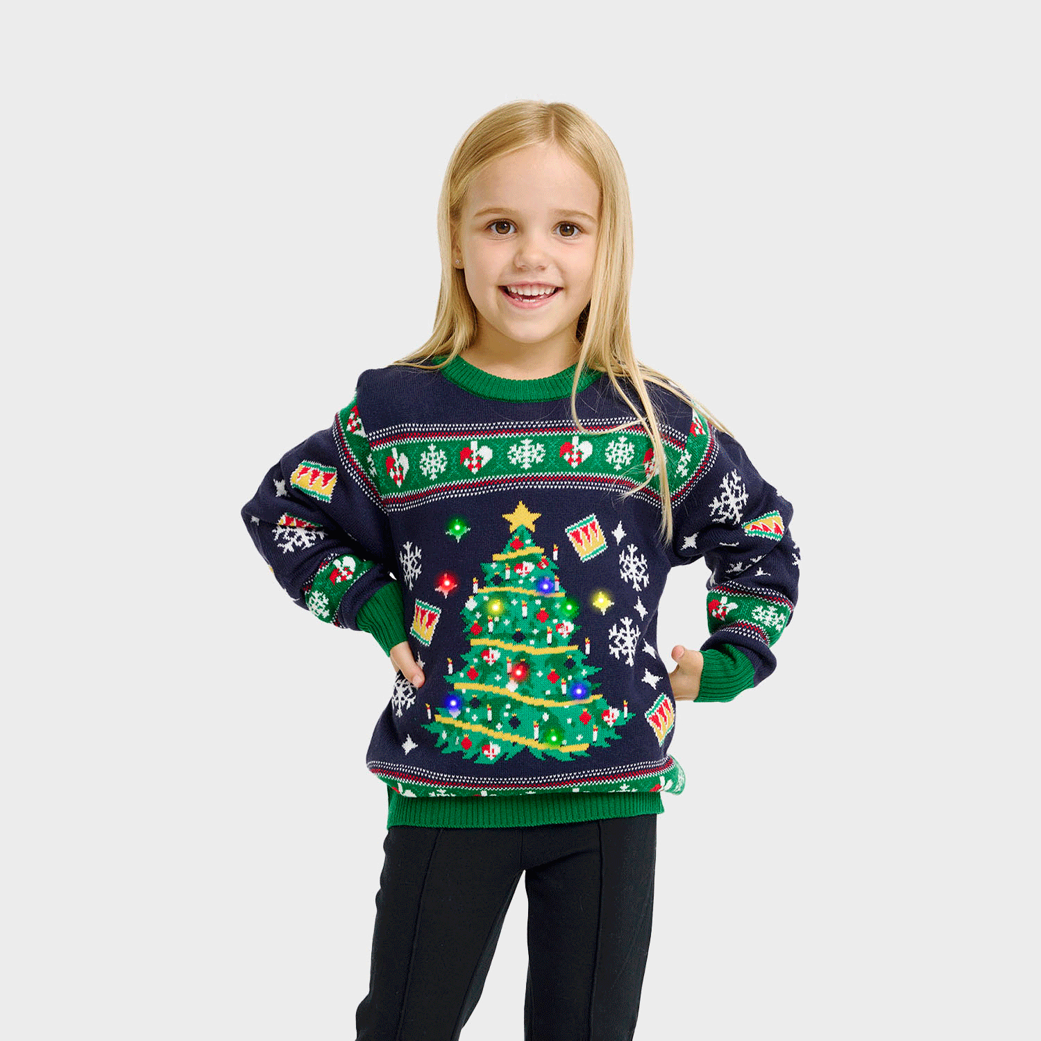 Een kind poseert in een blauwe en groene met een knipperende kerstboom.