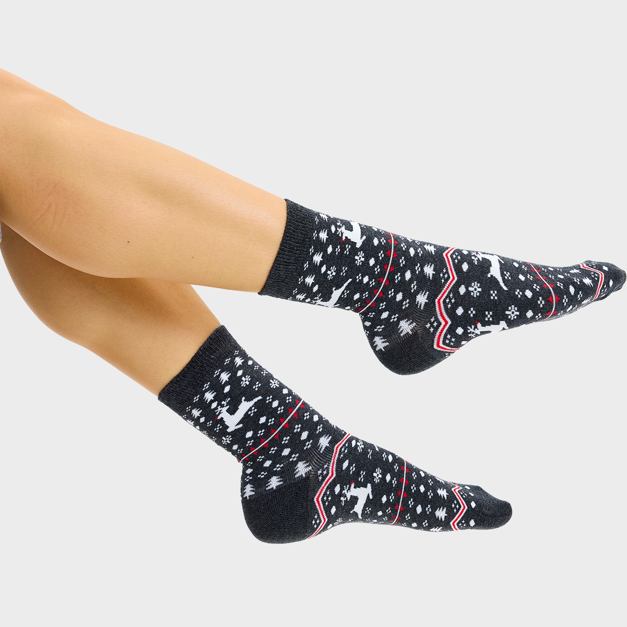 Een paar voeten met grijze kerstsokken met rendieren erop.