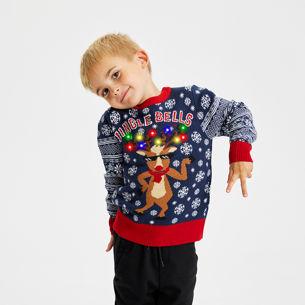 Een poserend kind dat een blauwe kersttrui draagt met een dansend rendier met lichtjes erop.