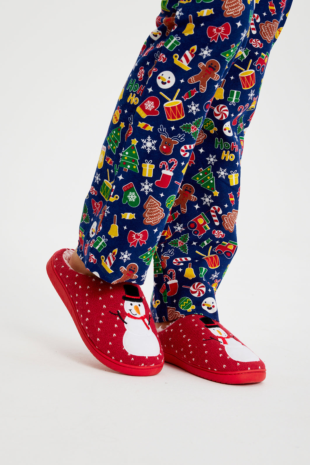 Un paio di gambe che indossano pantofole natalizie rosse con pupazzi di neve.