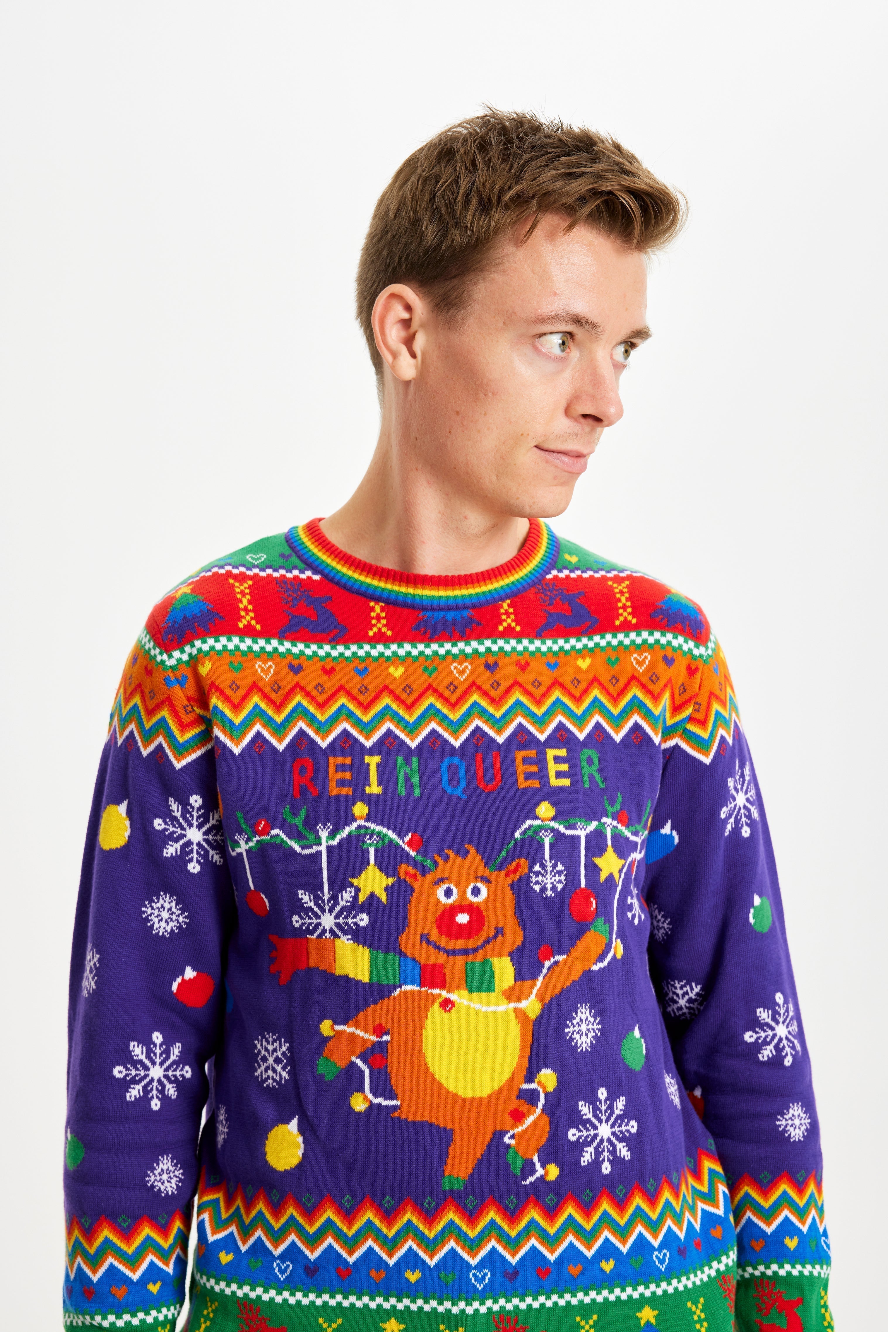 Un uomo guarda di lato e indossa un maglione natalizio color arcobaleno con la scritta 