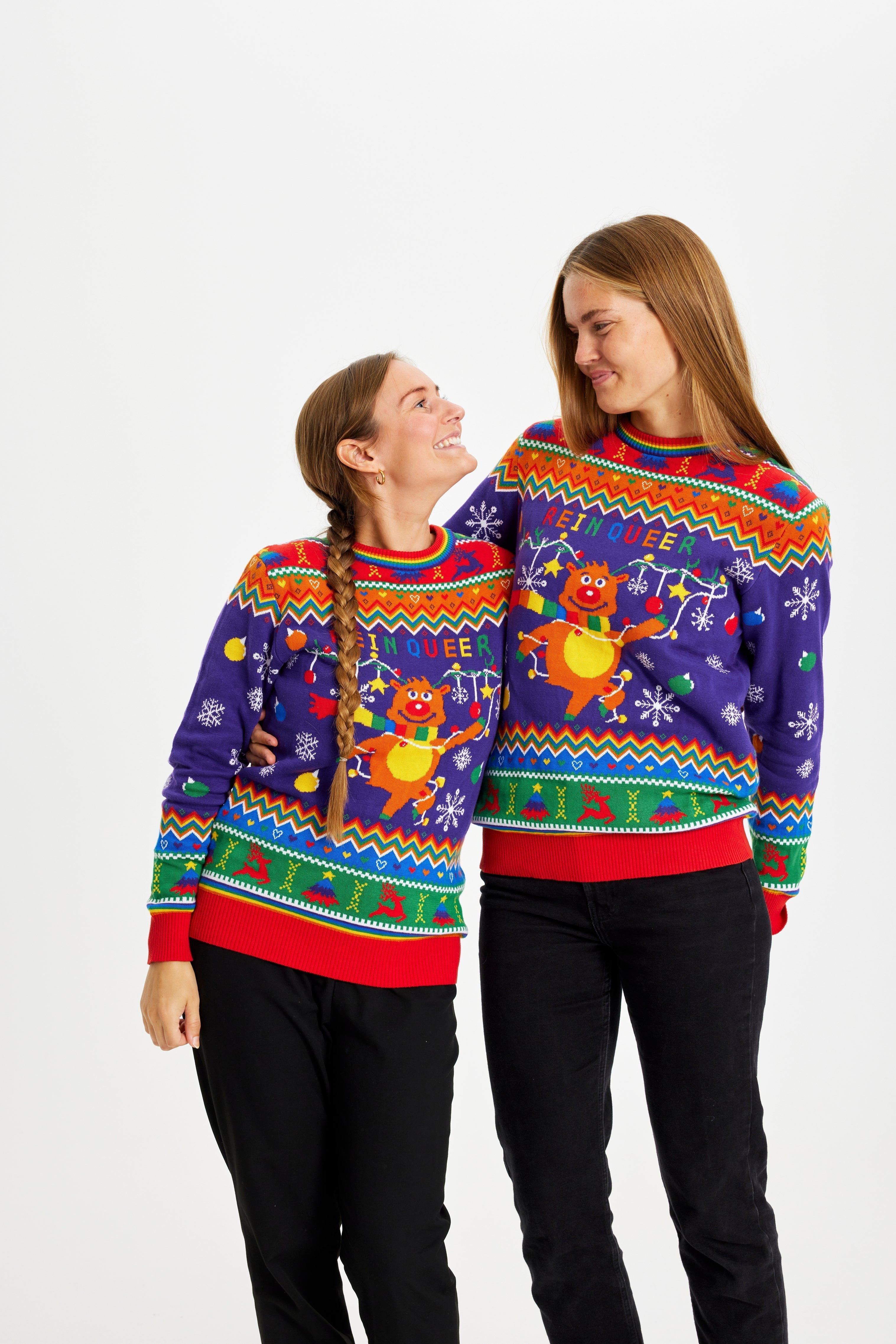 Due donne che indossano un maglione natalizio color arcobaleno con la citazione 