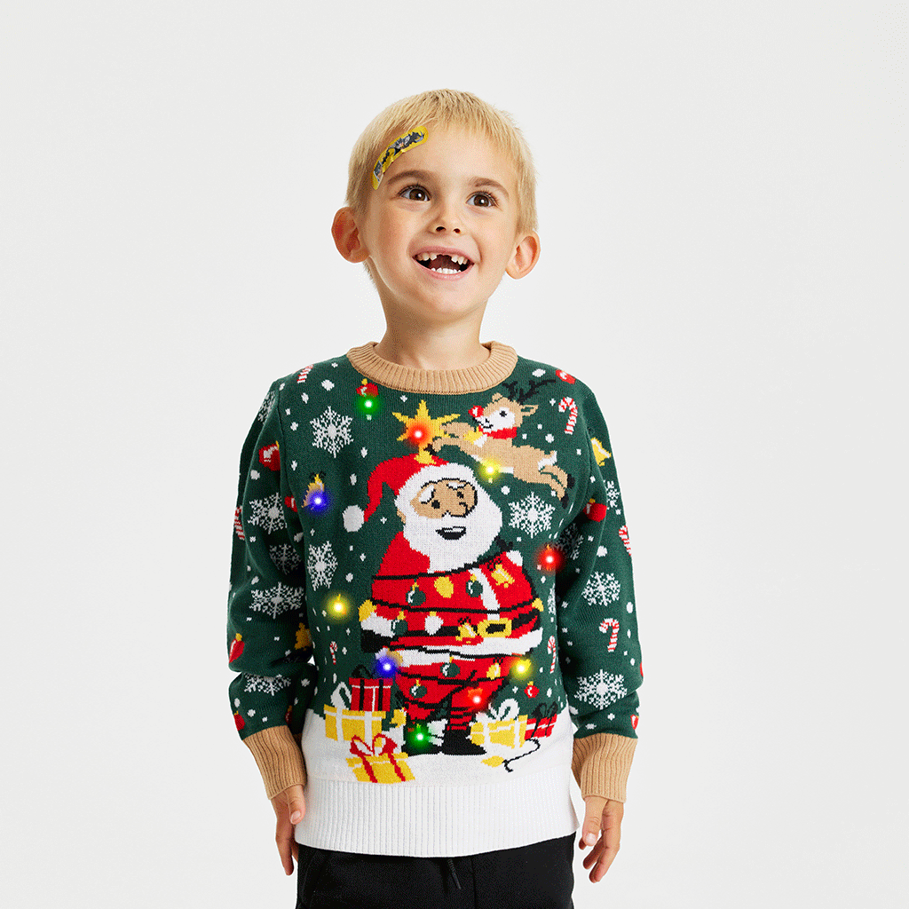 Un bambino in posa che indossa un maglione natalizio verde e bianco con Babbo Natale e luci.