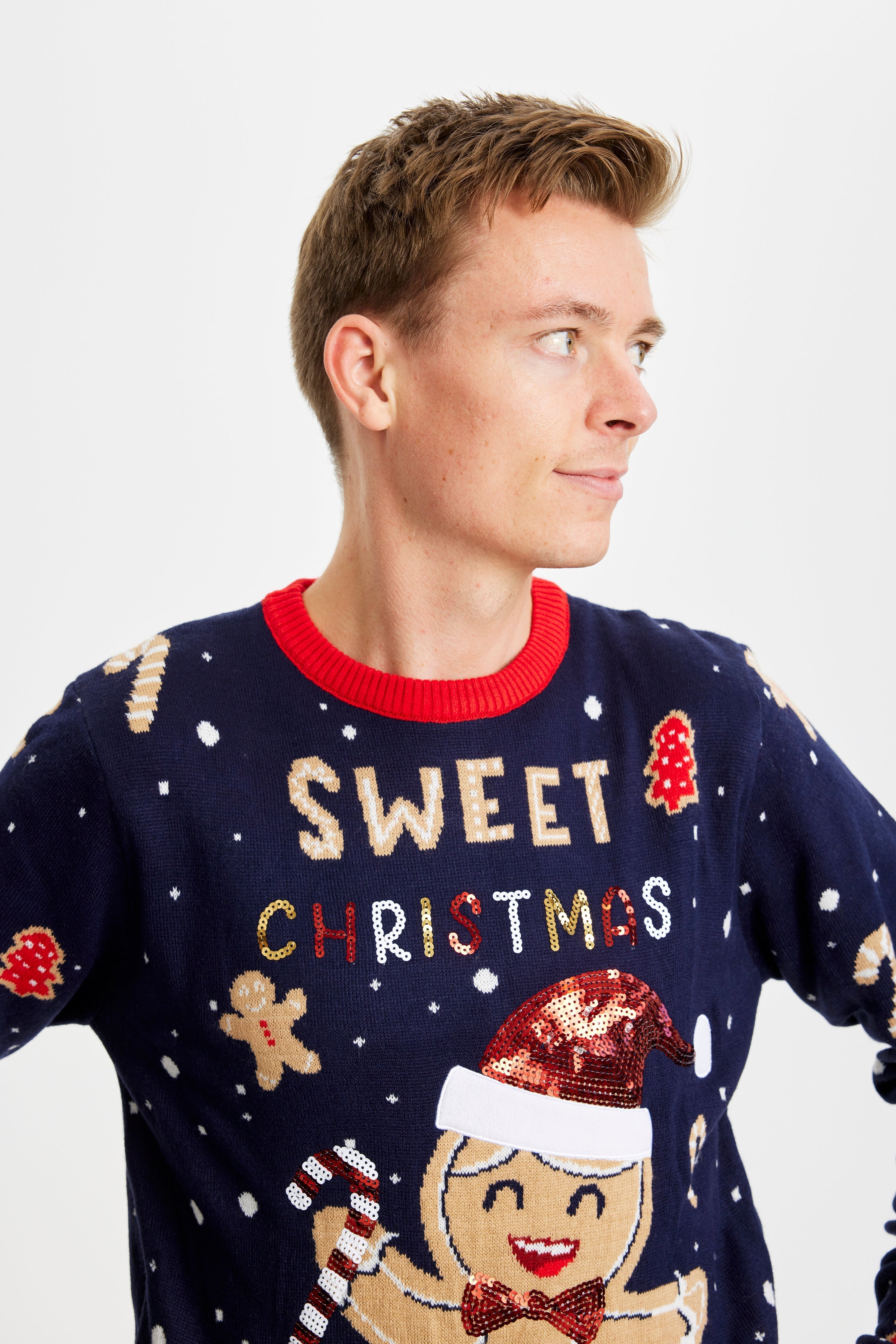 Un uomo guarda di lato e indossa un maglione natalizio blu con una torta e delle candeline.