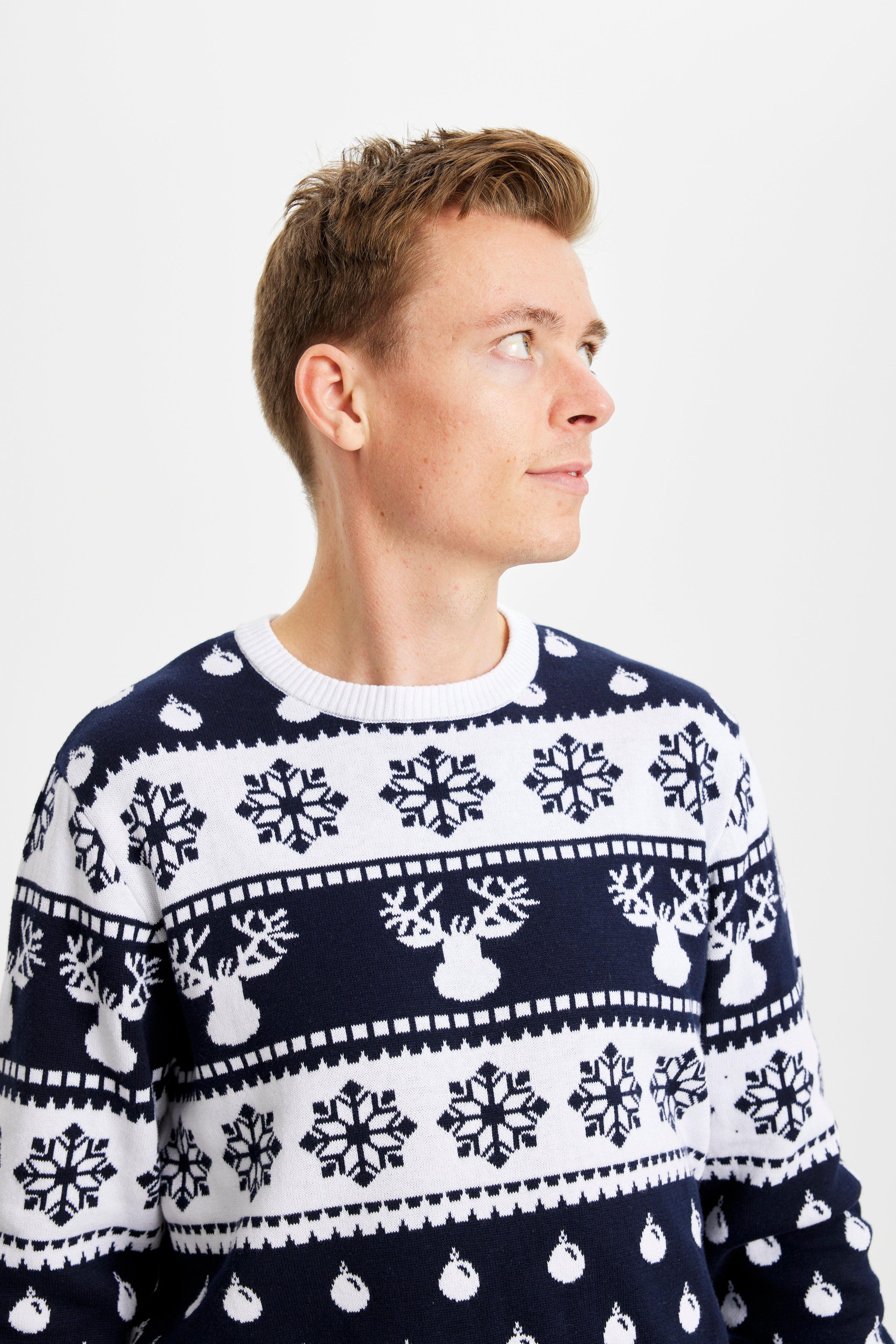 Un uomo posa indossando un maglione natalizio bianco e blu.