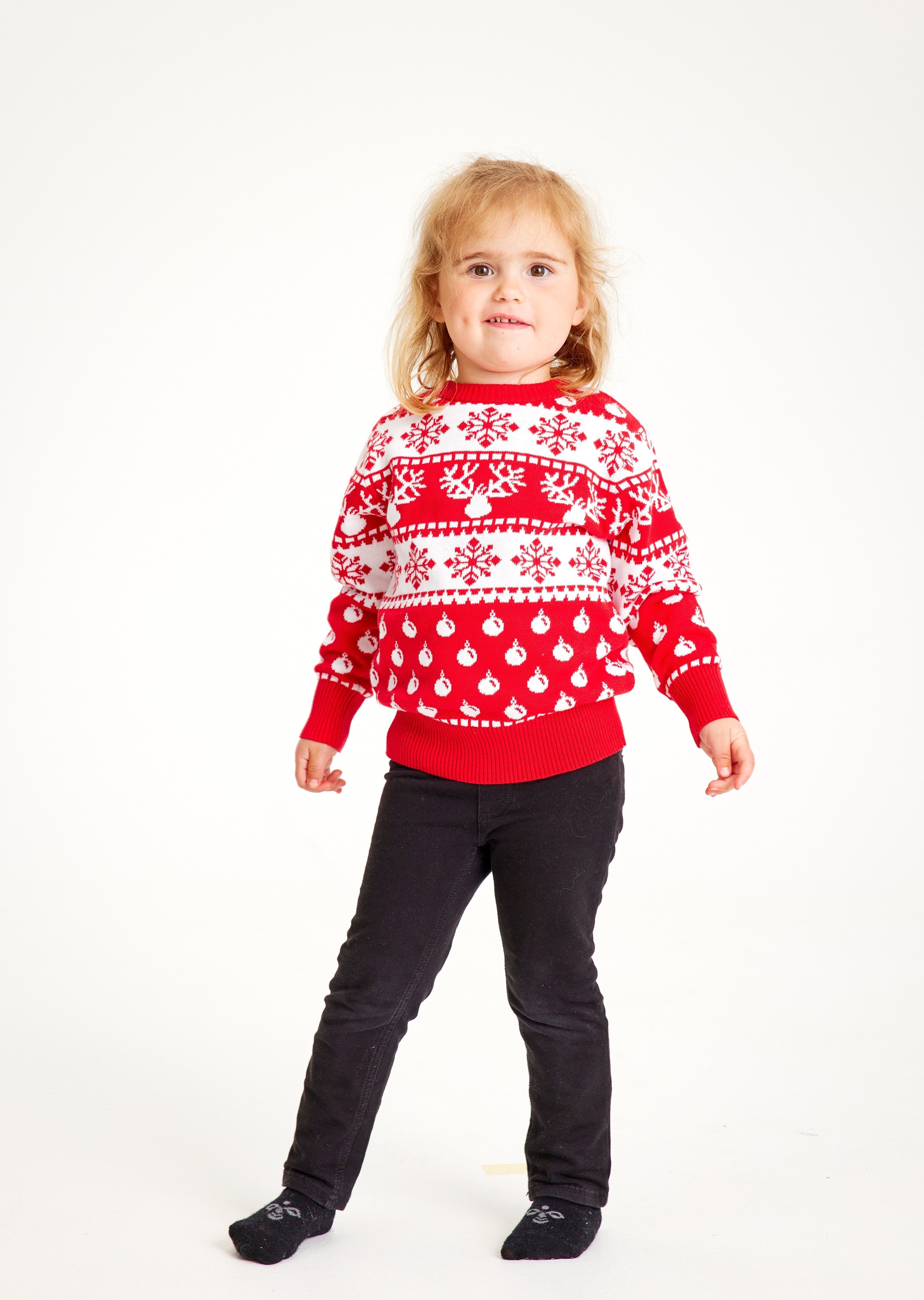 Un bambino posa indossando un maglione natalizio rosso.